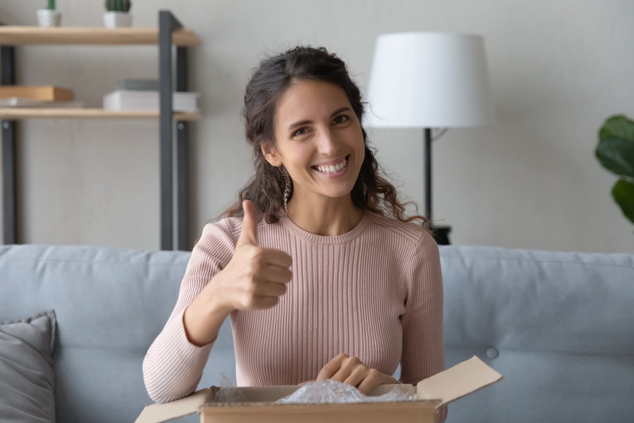 Woman sit with parcel box feels satisfied showing thumbs up